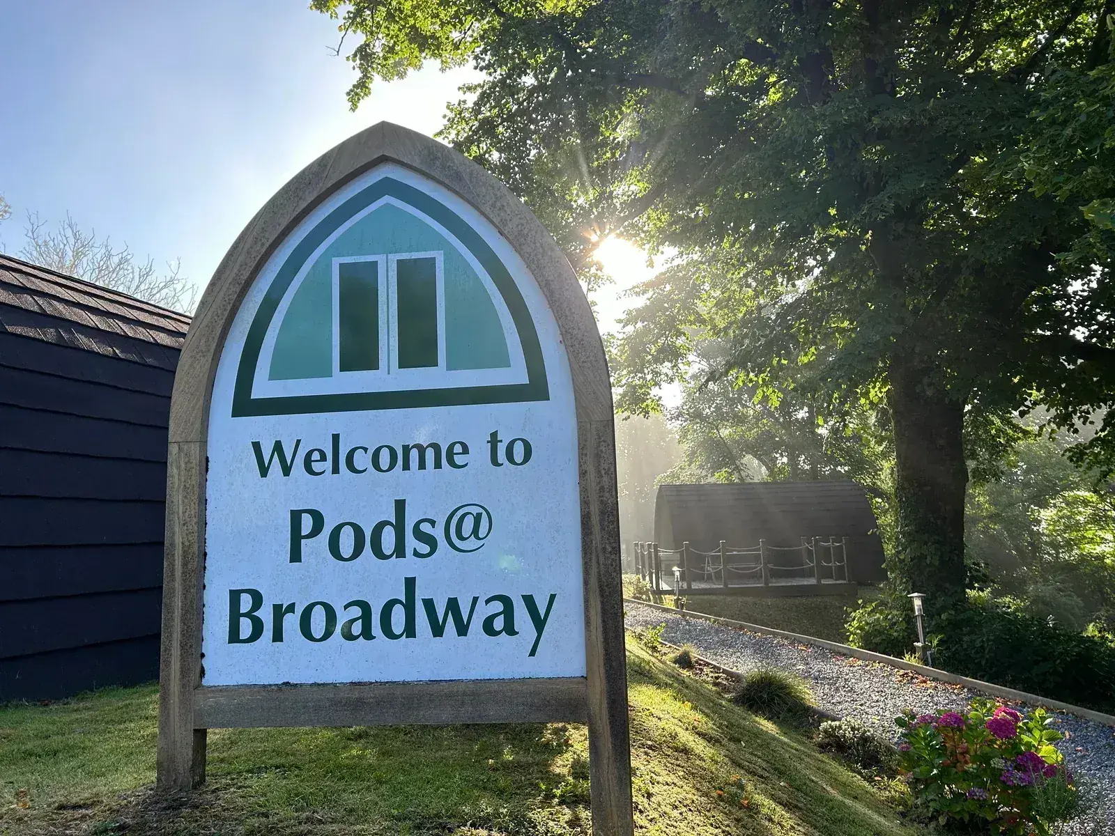 Welcome sign at Pods @ Broadway in morning sunlight with mist through the trees