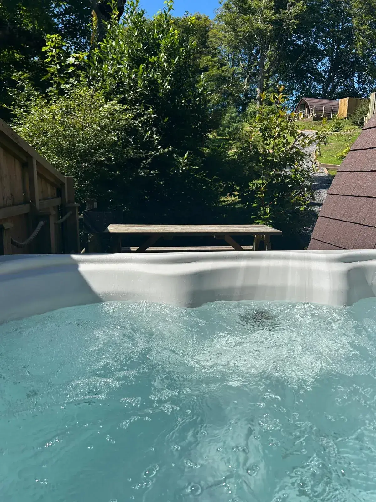 Private hot tub bubbling on a pod's decking, with a picnic table and countryside view beyond