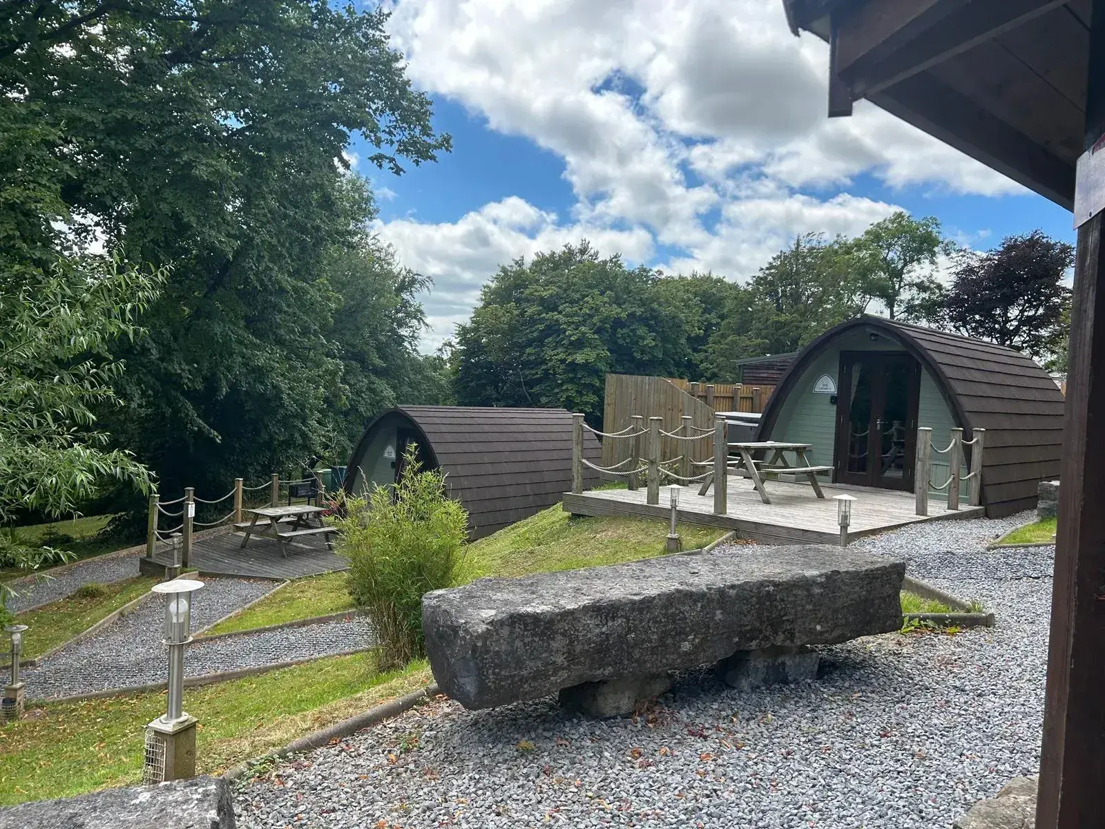 Jacuzzi Pods viewed from the grounds, with rope-railed decking and a stone bench in the foreground