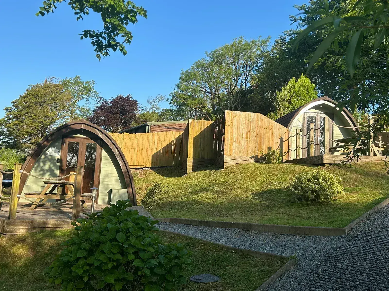 Two pods with lush summer greenery and new fencing — the full glamping site