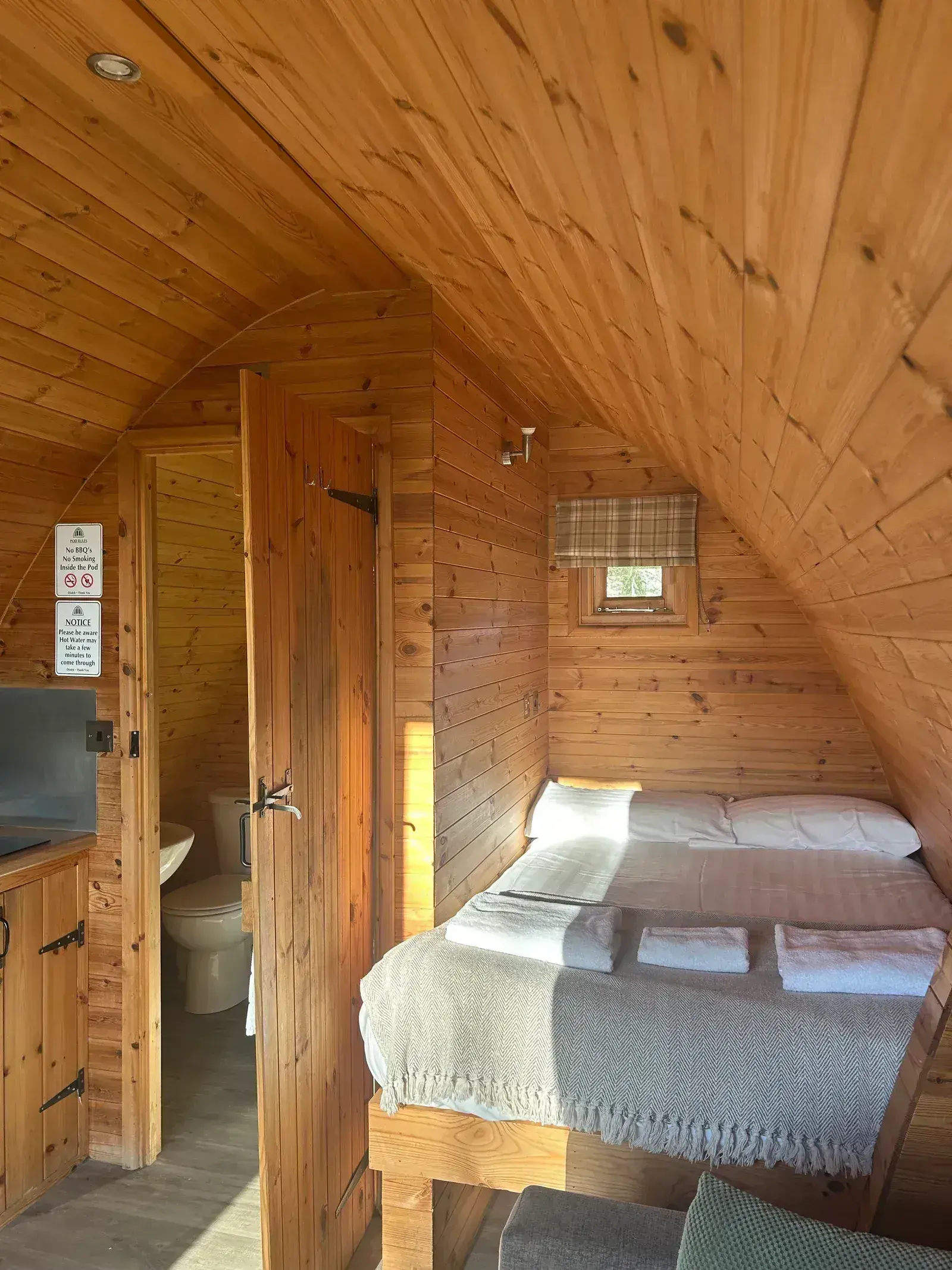 Cosy interior of a glamping pod — double bed beneath the curved pine ceiling with en-suite