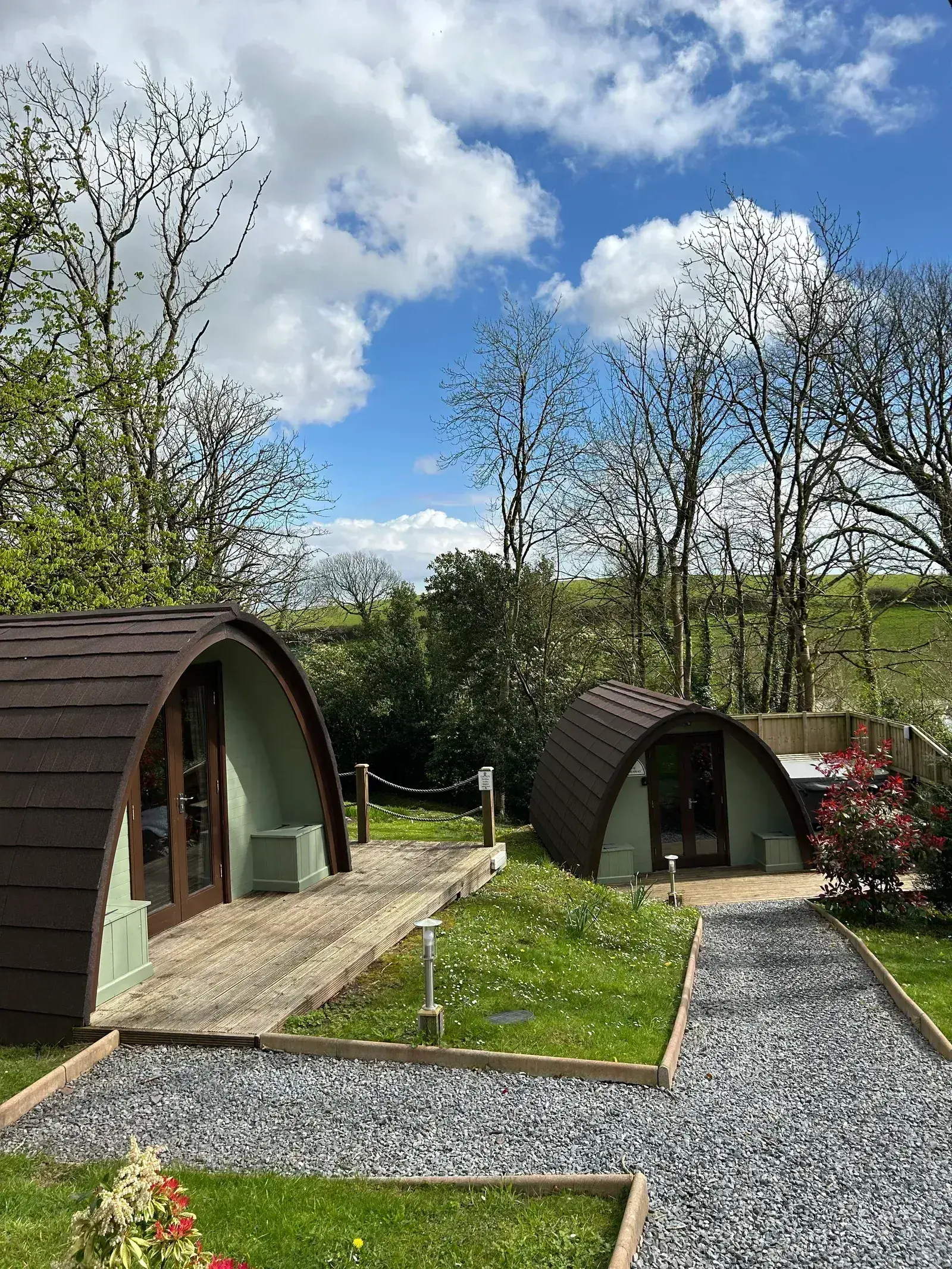 Two glamping pods with red spring flowers lining the gravel approach path