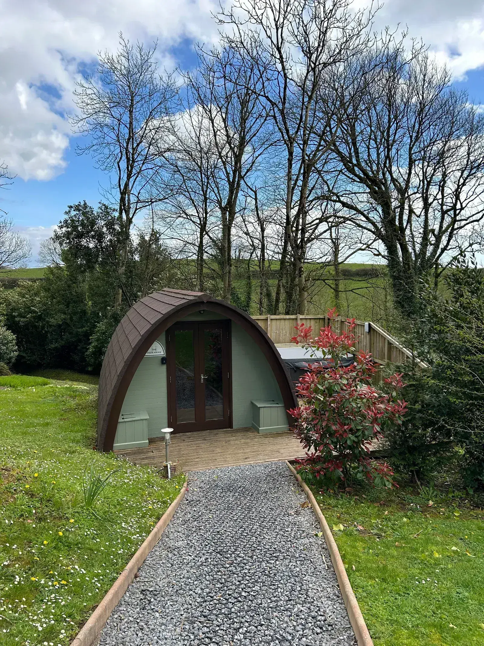 Glamping pod exterior with vibrant red flowers and sunny gravel pathway